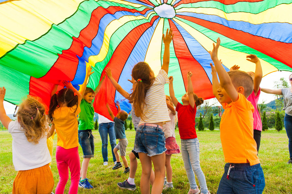 Joyous classmates jumping under colorful parachute at a Preschool & Daycare Serving Greenville, AL