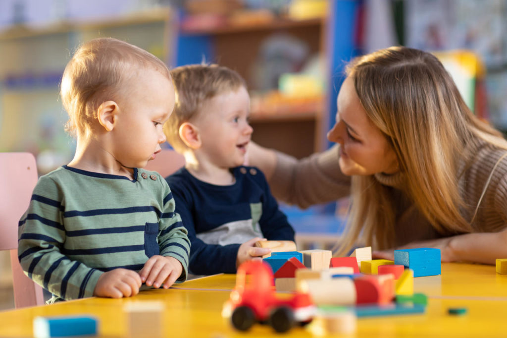 FAMILIES APPROACH nursery children building blocks with a teacher - Serving Greenville, AL